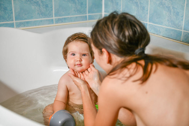 共同入浴の赤ちゃんとお母さん。ママの手は浴室で女の子を洗う。清潔・衛生教育の象徴. - 写真・画像
