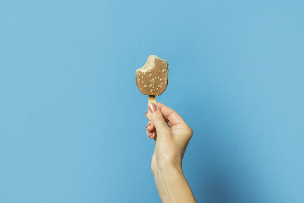 Naisten käsi pitää purettua jäätelöä kiinni sinisellä pohjalla. Kuuman kesän käsite, stressi. Tasainen, ylhäältä
 - Valokuva, kuva