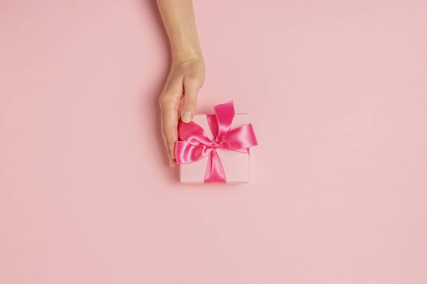 Female hands hold, take, receive a gift on a pink background. Wedding concept, Valentine's Day, a gift for a loved one. Flat lay, top view - Photo, Image
