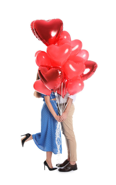 Young couple hiding behind heart shaped balloons isolated on white. Valentine's day celebration - Foto, Imagen