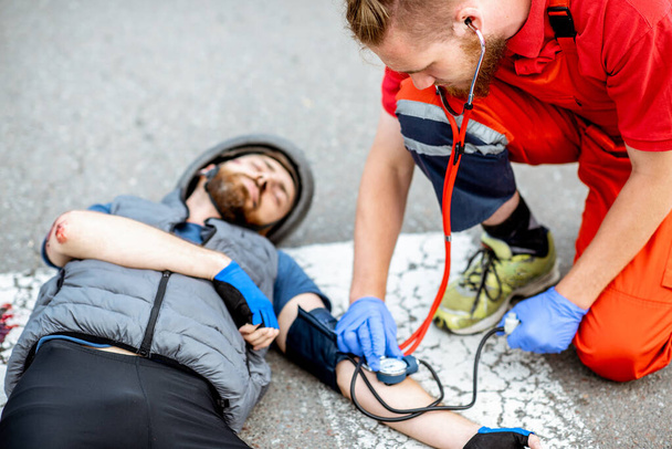 Medic applying first aid to the injured man on the road - Photo, Image
