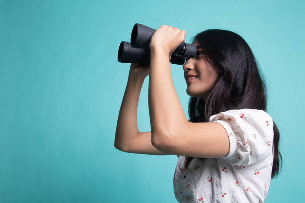 Young Asian woman with binoculars  on cyan background - Foto, Imagem