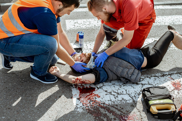 Medics applying emergency care to the injured man on the road - Foto, afbeelding