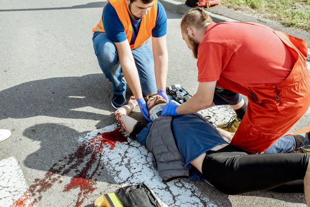 Sağlık ekipleri yoldaki yaralı adama acil bakım uyguluyor. - Fotoğraf, Görsel