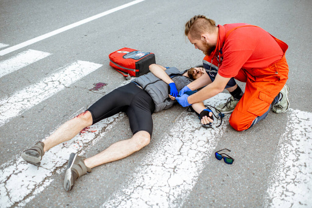 Sanitäter leisten dem Verletzten auf der Straße Erste Hilfe - Foto, Bild