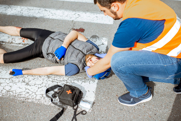 Accidente de tráfico con ciclista lesionado y hombre que proporciona primeros auxilios
 - Foto, imagen