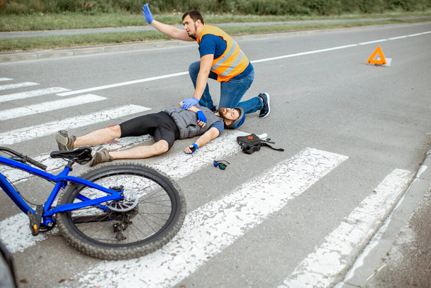 Accidente de tráfico con ciclista lesionado y hombre que proporciona primeros auxilios
 - Foto, imagen