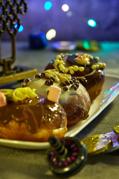 Еврейский праздник Ханука фон. Традиционное блюдо сладкие пончики. Крутящиеся топы на синем фоне и ханукальный гелт, который обычно раздают детям на праздники
 - Фото, изображение