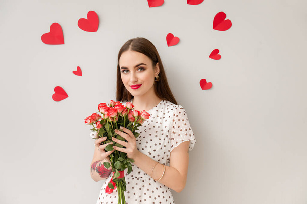 Beautiful young woman with bouquet of flowers and hearts on light background. Valentine's Day celebration - Foto, Bild