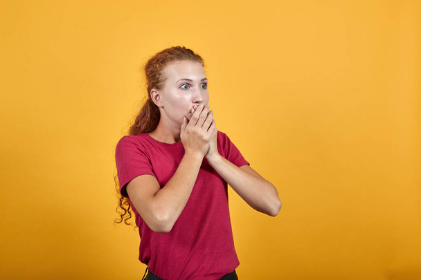 Scared young lady in red shirt covering mouth with hand, looking frightened - Photo, Image