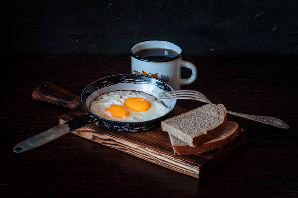 Fried scrambled eggs in a vintage pan, with bread, metal mug with tea - Photo, image