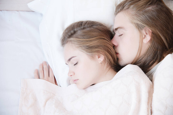 Close-up van een jong echtpaar in bed, slapend in een omhelzing, verstopt achter een deken. Het concept van een jong gezin en gezonde slaap - Foto, afbeelding