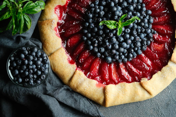 Homemade backing. Delicious galette with plums and blueberries on a dark background copy space top view - Valokuva, kuva