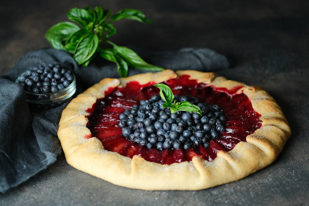 Homemade backing. Delicious galette with plums and blueberries on a dark background copy space. - Photo, Image