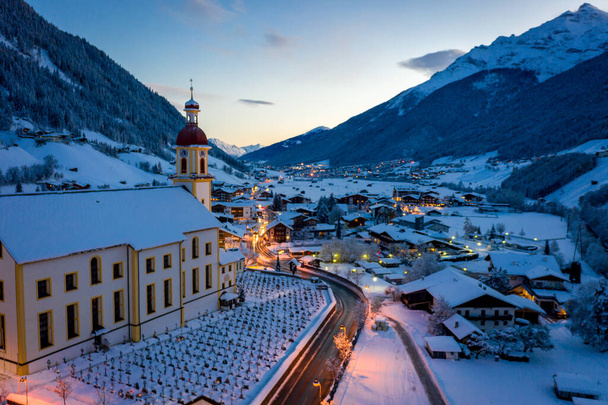 Cidade da manhã de inverno na cidade austríaca de Neustift. Vista aérea do centro da cidade e da igreja. Iluminação matinal de casas e semáforo. Tirol, Vale do Stubai
 - Foto, Imagem