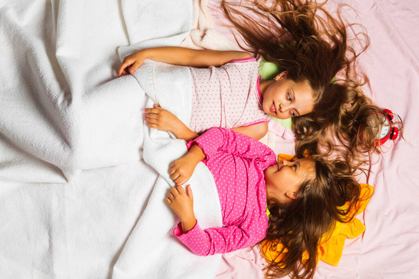Kids in pink pajamas covered with white blanket. - Foto, afbeelding