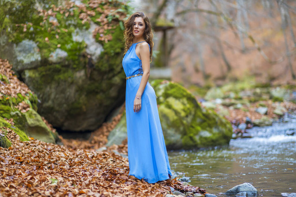 Sonbahar günü nehrin kenarında mavi elbiseli bir kadın. - Fotoğraf, Görsel