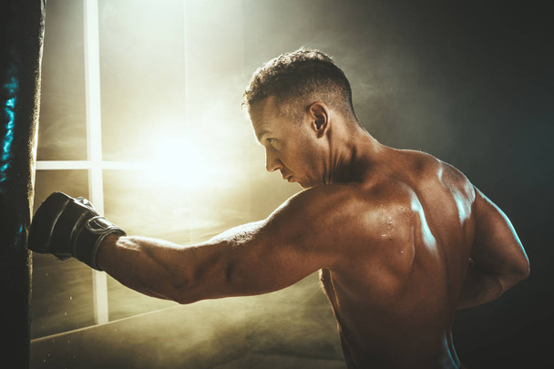 Концентрированный мускулистый человек активно и упорно тренируется, ударяясь о боксерскую грушу
. - Фото, изображение