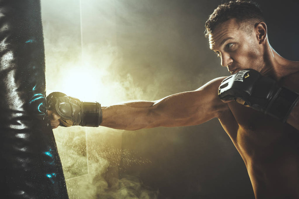 El hombre muscular concentrado está entrenando activa y duro, golpeando un saco de boxeo
. - Foto, Imagen