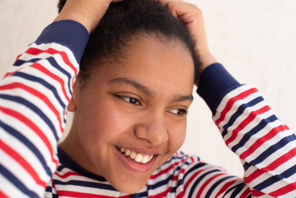 Close up retrato de sorrir jovem menina afro-americana com as mãos no cabelo
 - Foto, Imagem