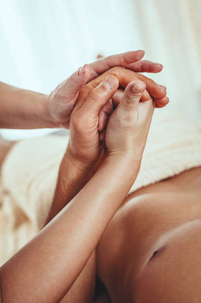 Close-up van een hads van jonge vrouwelijke therapeut masseren palm van jonge man in schoonheidssalon.   - Foto, afbeelding