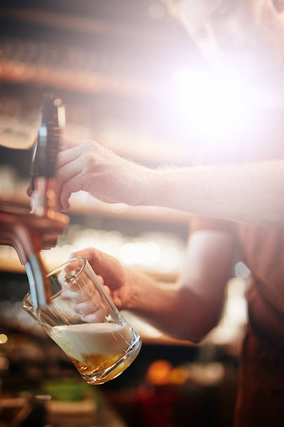 Przystojny biały barman nalewający piwo stojąc w pubie. Selektywne skupienie uwagi na dłoni. - Zdjęcie, obraz