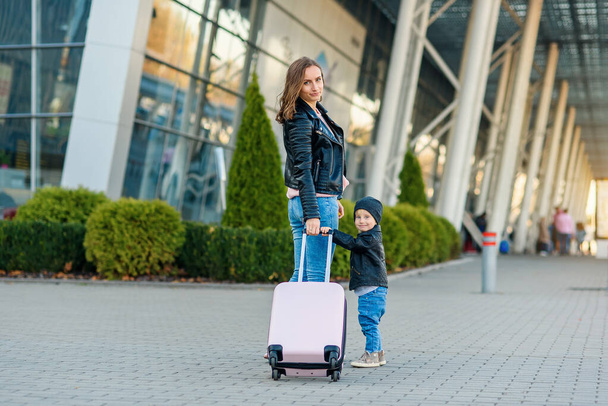 Beautiful mother and her stylish cute daughter walk together and pull a pink suitcase to the airport. - Foto, Imagen