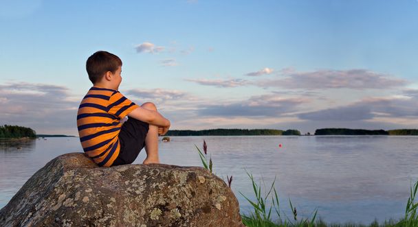 夏の夜の日光の岩の上に座っている少年のパノラマ - 写真・画像