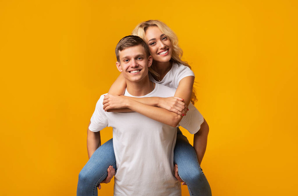 glimlachende jonge kerel dragen vriendin op zijn rug - Foto, afbeelding