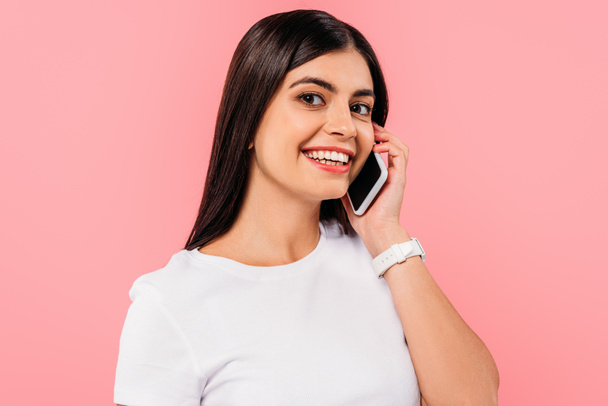 smiling pretty brunette girl talking on smartphone isolated on pink - Foto, Imagen