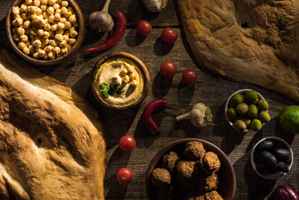 вид на вкусный фалафель, хумус, горох, питу, овощи и оливки на деревянном деревенском столе
 - Фото, изображение
