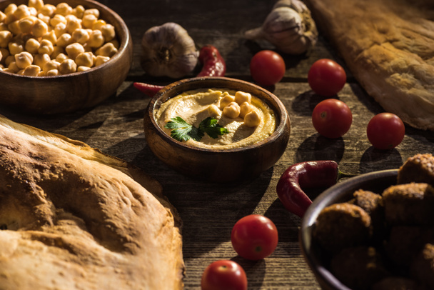 delicious falafel, hummus, chickpeas, pita, vegetables and spices on wooden rustic table - Фото, зображення
