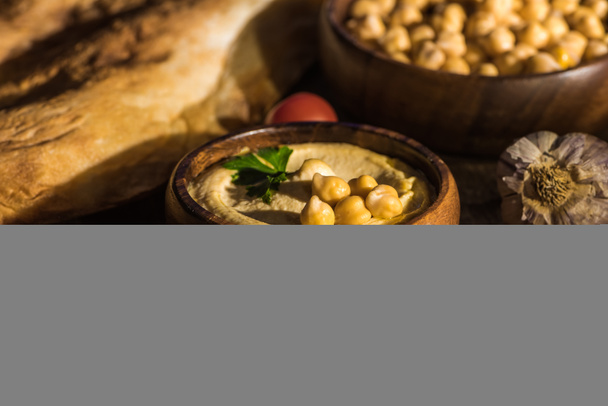 selective focus of delicious hummus, chickpeas, pita, vegetables and spices on wooden rustic table - Фото, изображение