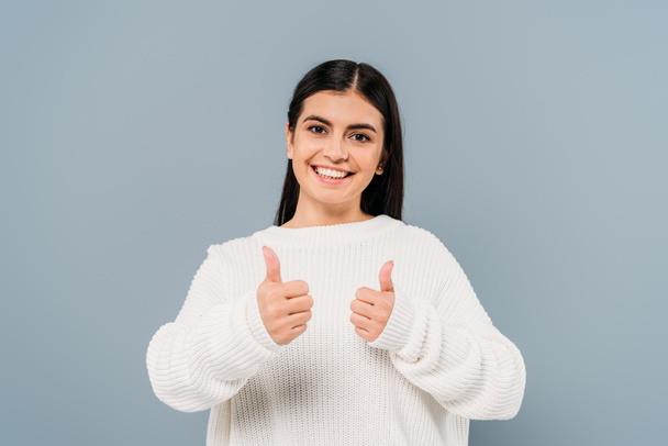 happy pretty brunette girl in white sweater showing thumbs up isolated on grey - Фото, изображение