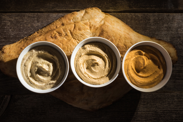 top view of delicious assorted hummus on fresh baked pita on wooden rustic table - Photo, Image