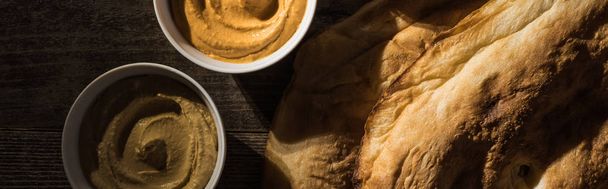 top view of delicious assorted hummus near fresh baked pita on wooden rustic table, panoramic shot - Fotografie, Obrázek