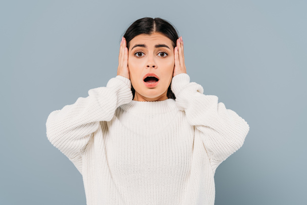 shocked pretty brunette girl in white sweater covering ears isolated on grey - Photo, Image
