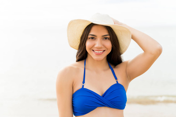 Mulher sorridente bonita usando chapéu e biquíni desfrutando na praia
 - Foto, Imagem