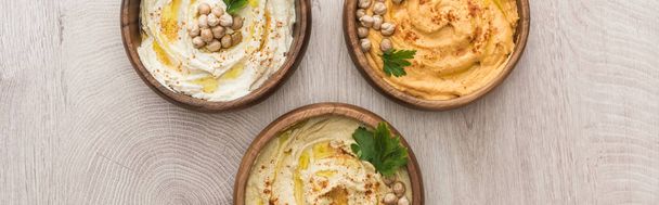 top view of delicious hummus with chickpeas in bowls on beige wooden table, panoramic shot - Foto, Imagen