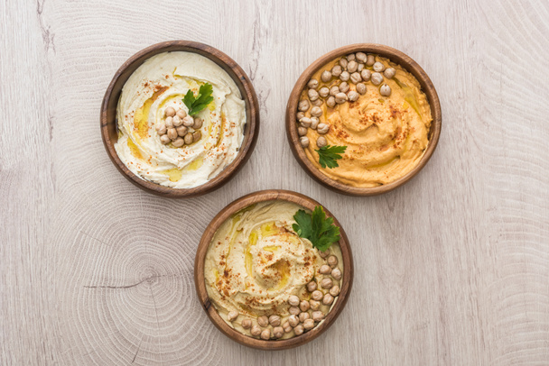 top view of delicious hummus with chickpeas in bowls on beige wooden table - Photo, Image