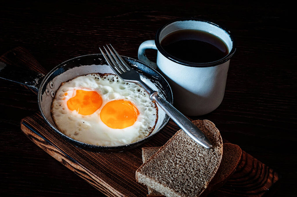 パン、古いフォーク、紅茶と金属製のマグカップ、サイドビュー、暗い背景で、ヴィンテージパンでスクランブルエッグを揚げ - 写真・画像