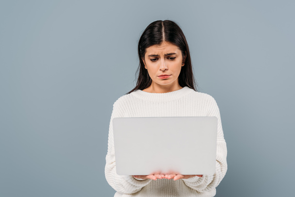 sad pretty brunette girl in white sweater holding laptop isolated on grey - Photo, Image