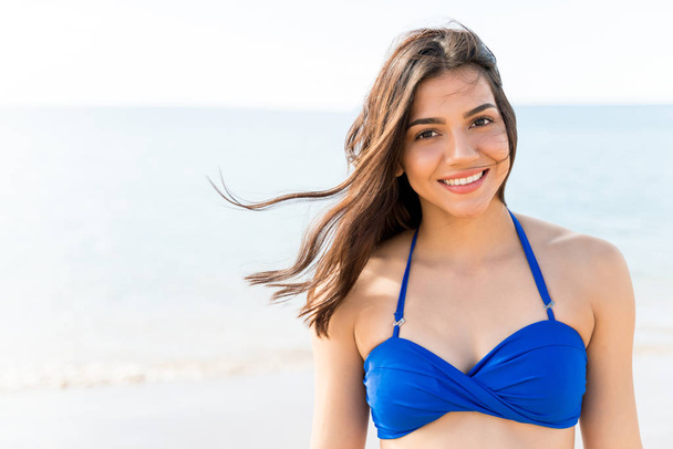 Atraktivní usmívající se žena v modrých bikinách těší vítr na pláži - Fotografie, Obrázek