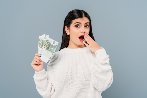 потрясена красивая девушка в белом свитере, держащая банкноты евро изолированные на сером
 - Фото, изображение