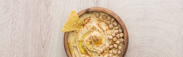 top view of delicious hummus with chickpeas and nacho in bowl on beige wooden table, panoramic shot - Valokuva, kuva