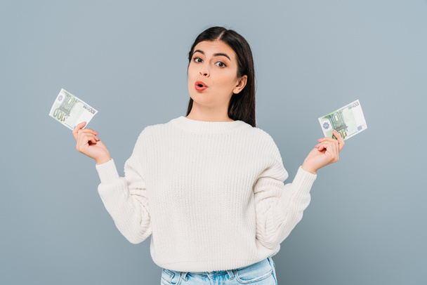 surprised pretty girl in white sweater holding euro banknotes isolated on grey - Fotografie, Obrázek