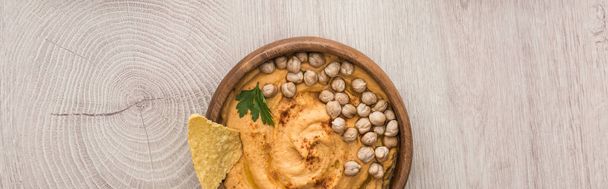vista superior del delicioso hummus con garbanzos y nacho en cuenco sobre mesa de madera beige, plano panorámico
 - Foto, Imagen