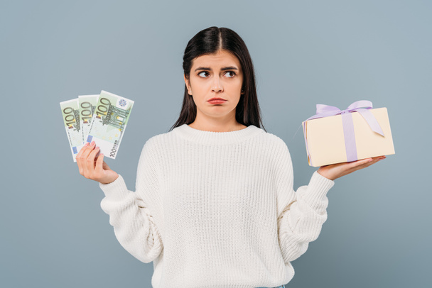 sad pretty girl in white sweater holding euro banknotes and gift box isolated on grey - Фото, зображення
