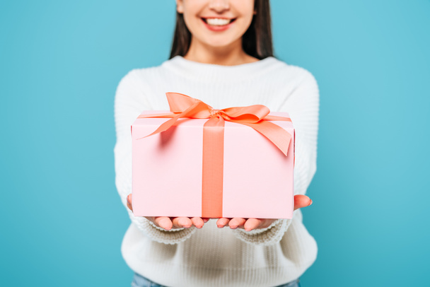 recortado vista de sonriente chica bonita en suéter blanco presentando caja de regalo aislado en azul
 - Foto, Imagen