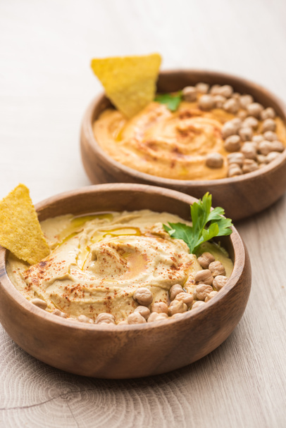 selective focus of delicious hummus with chickpeas and nacho in bowls on beige wooden table - Photo, Image